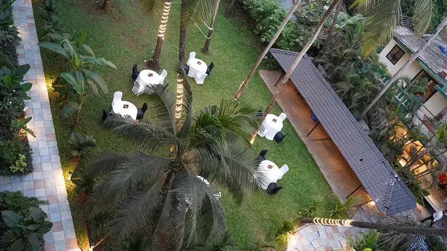 Aerial view of an open-air banquet space in the lawn with comfortable chairs around tables at Indie Stays Resort, Goa.