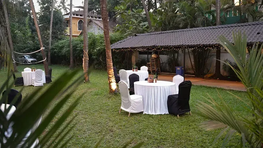 An open-air banquet space in the lawn with comfortable chairs around tables at Indie Stays Resort, Goa.