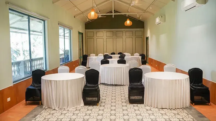 A conference hall set up with chairs around tables at Indie Stays Resort, Goa.