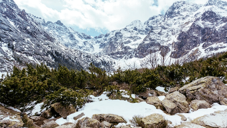 A mountainous landscape with snow-covered rocks and a small, frozen lake.