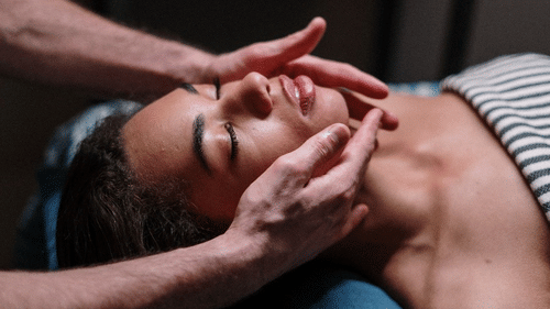 a person with closed eyes receiving a relaxing facial massage, with the hands of the therapist gently massaging their face