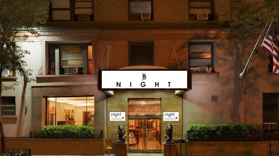 Exterior view of Night Hotel Broadway, showing the main entrance with a lit signboard and American flag on the side.