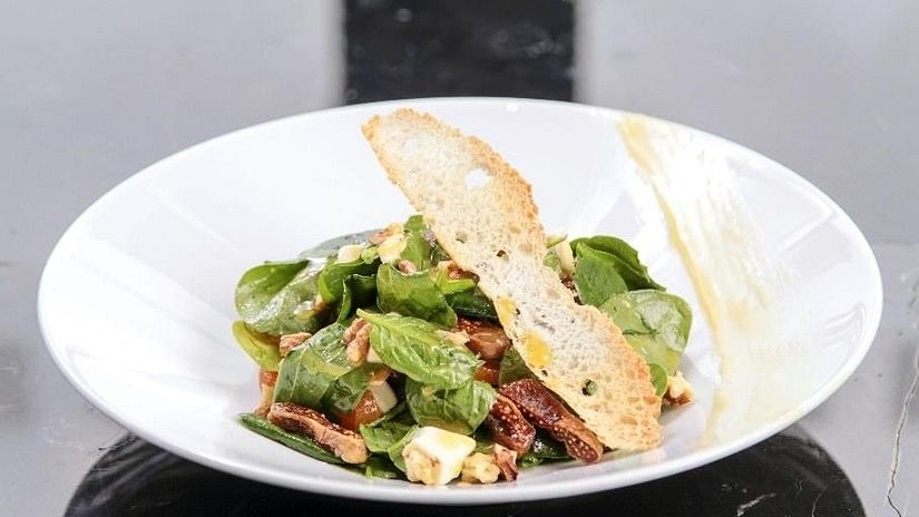 A gourmet spinach salad with bacon, feta, and a slice of toasted bread, elegantly presented on a white plate at YO1 Longevity & Health Resorts, Catskills