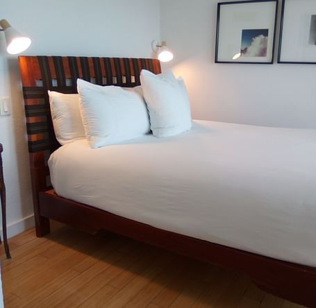 Bed with white linens and wooden headboard at Casa Morada, shown from a side angle.