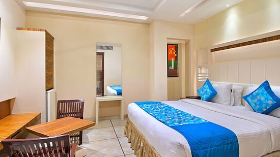 Super Deluxe Room at Hotel Hari Piorko featuring a plush ed with fresh linen and blue bed runner along with cushions and its reflection partially visible on the mirror next to it on the wall