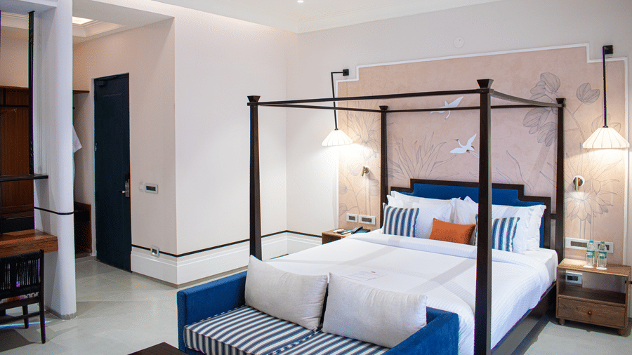 Elegant four-poster bed with a botanical mural and a cosy seating nook at The Sierra, Udaipur.