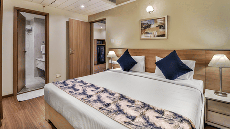Bedroom of a Deluxe Suite at Starlit Suites Newtown, Kolkata, featuring a neatly-made bed, matching nightstand, and an attached bathroom.