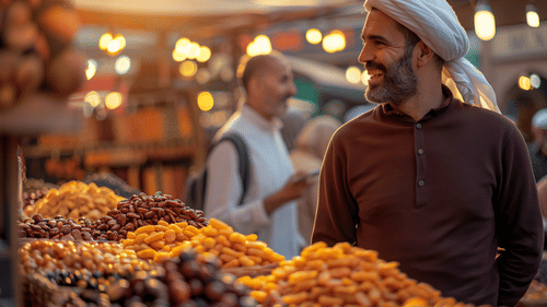 A man looking at a shopkeeper with a display of various dry fruits and spices in the background.