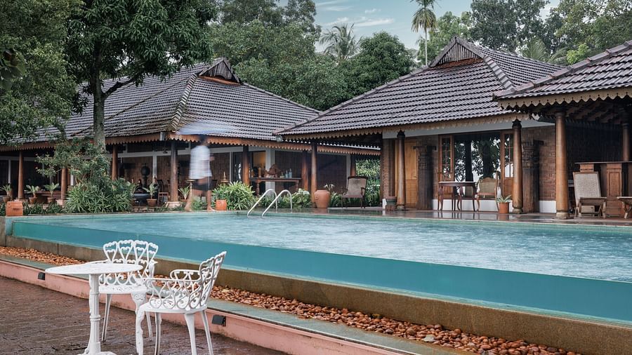 A shot of the pool with chairs and table near it and the restaurant in the background - BluSalzz Villas - Muhamma Resort, Alleppey