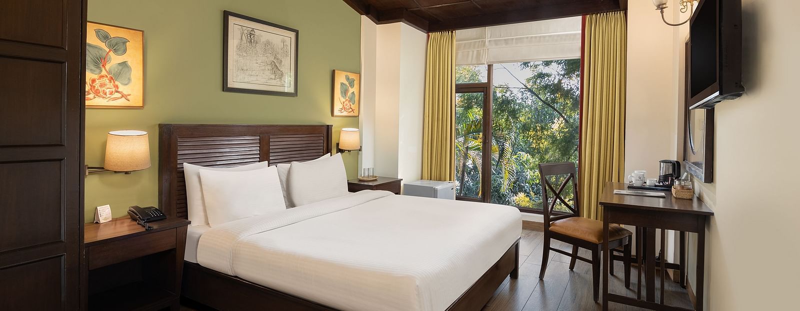 An image of a bedroom with double size bed, bedside table on either side, photos hanged on the wall and four windows from which natural lights are coming in - The Riverview Retreat,  Corbett