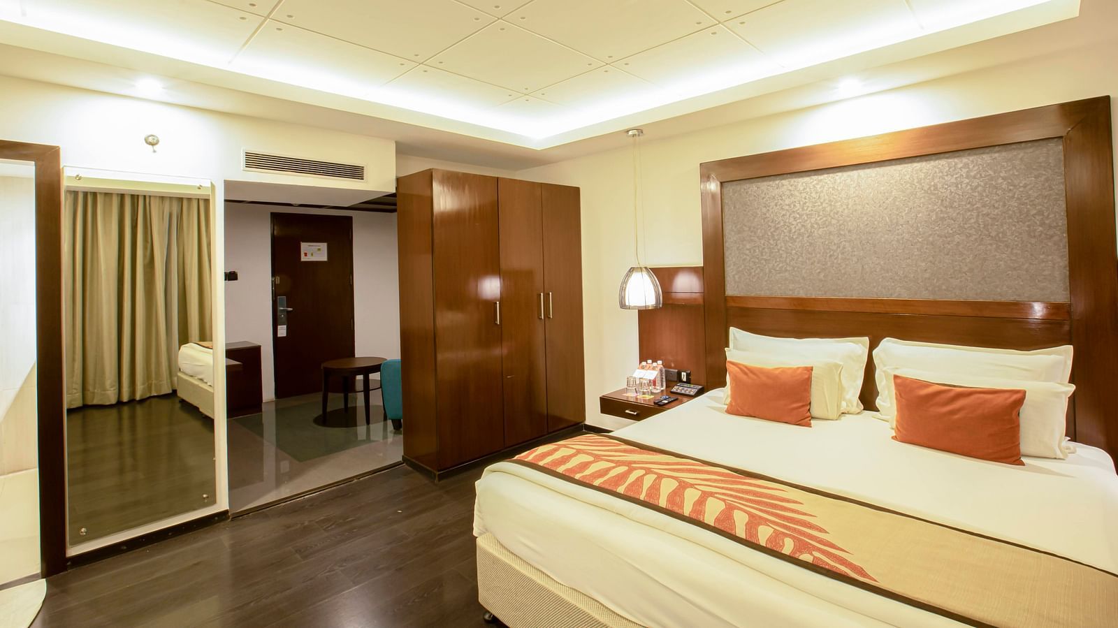 Studio Room at The Cunningham Hotel with warm lighting, a plush bed with a large headboard and a mirror attached to wall next to the wardrobe