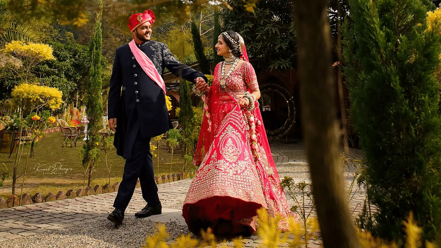 A photo shoot of a bride and groom walking on a pathway surrounded by greenery.