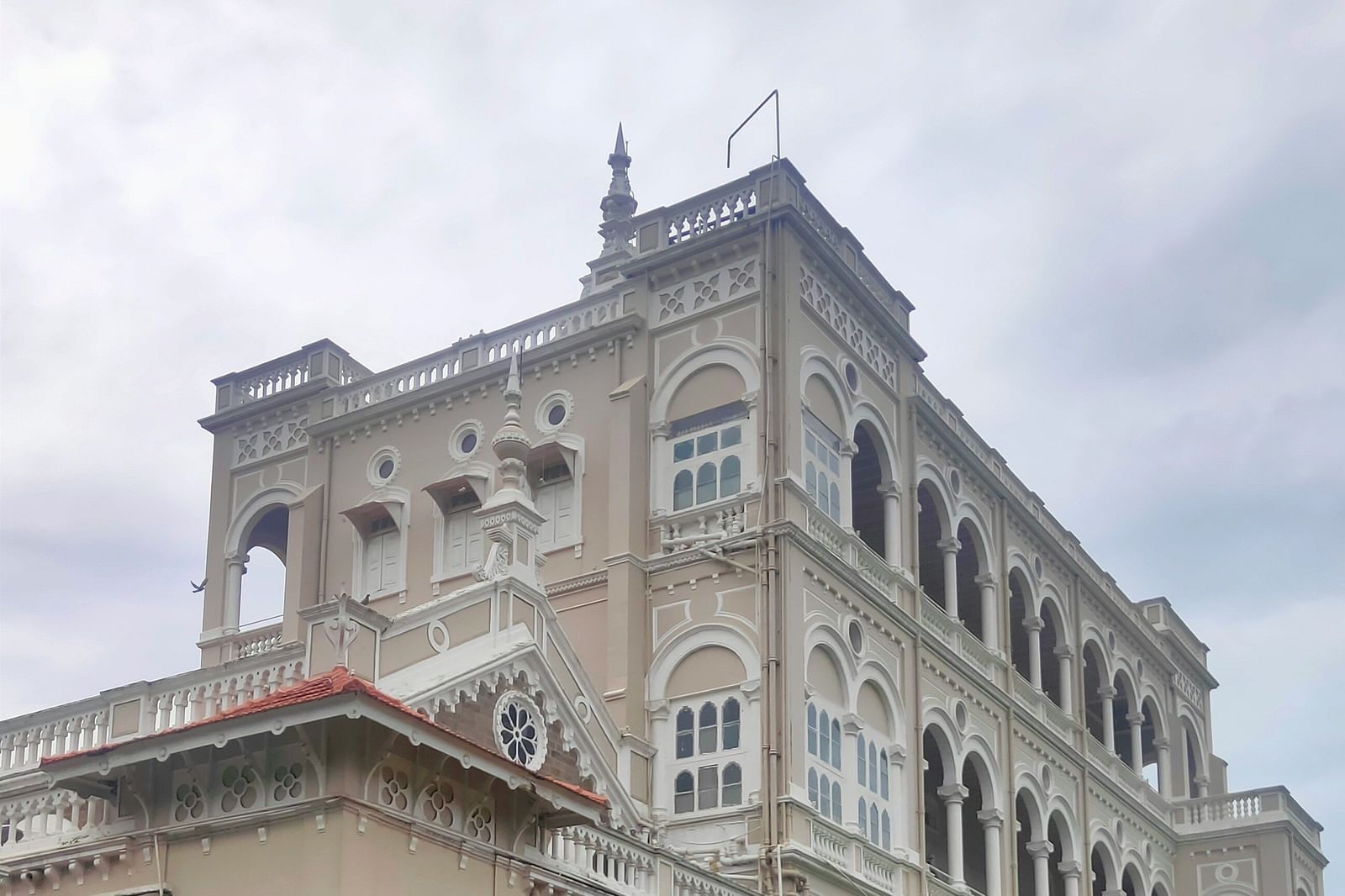Grand heritage building with arched windows, tiled roof, and garden area.