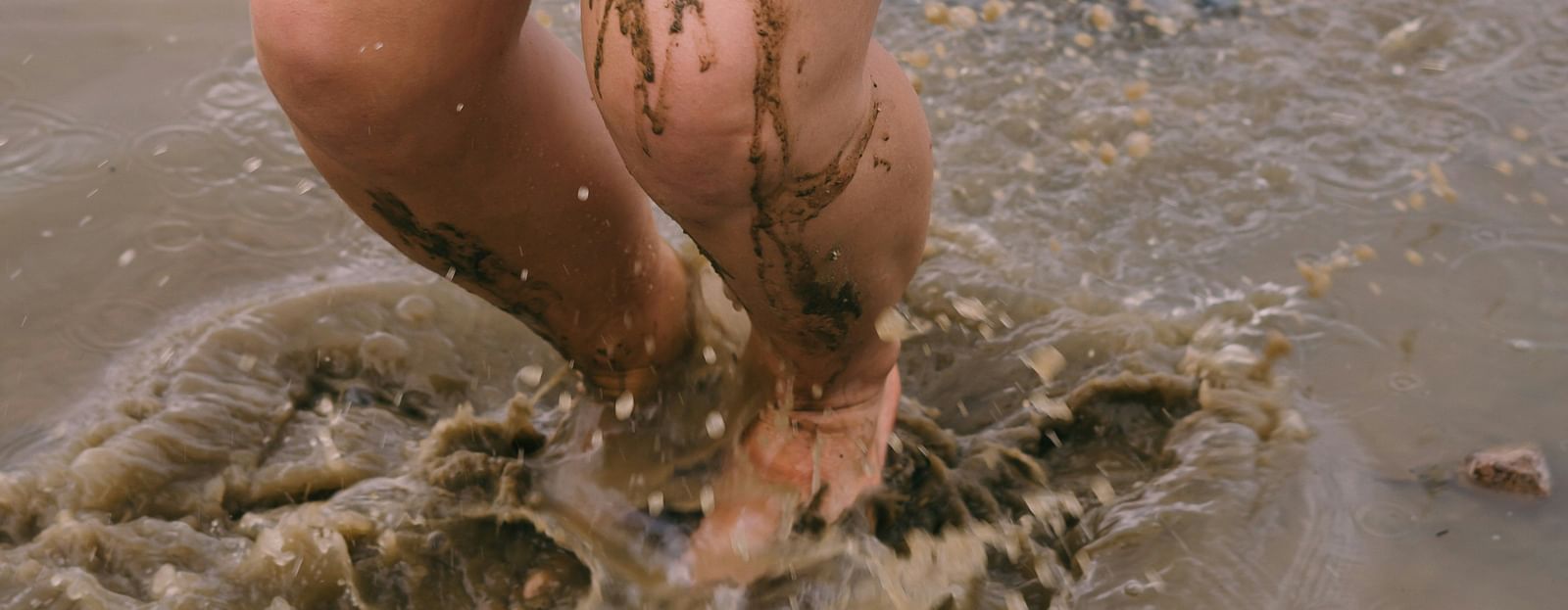 A close up of a person jumping on a pool of muddy waters with droplets flying around - Nha Trang Mud Baths Hot Springs