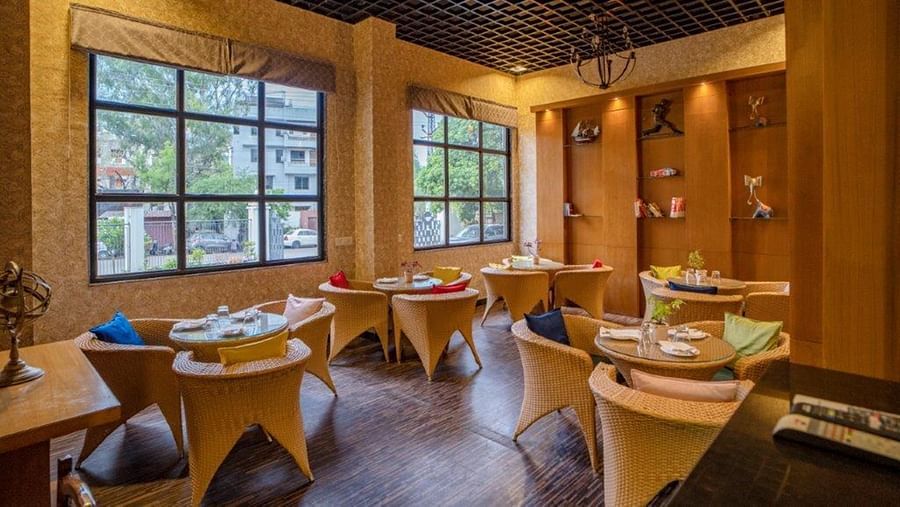 Dining area with wooden furniture and large glass windows at Golden Tulip, Udaipur.