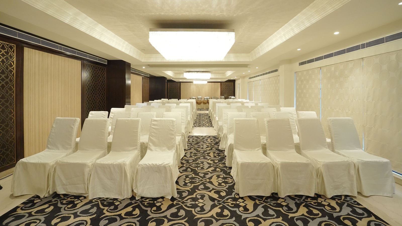 A spacious event hall with many chairs covered in white fabric, arranged on a patterned carpet - Fragrant Nature Cochin