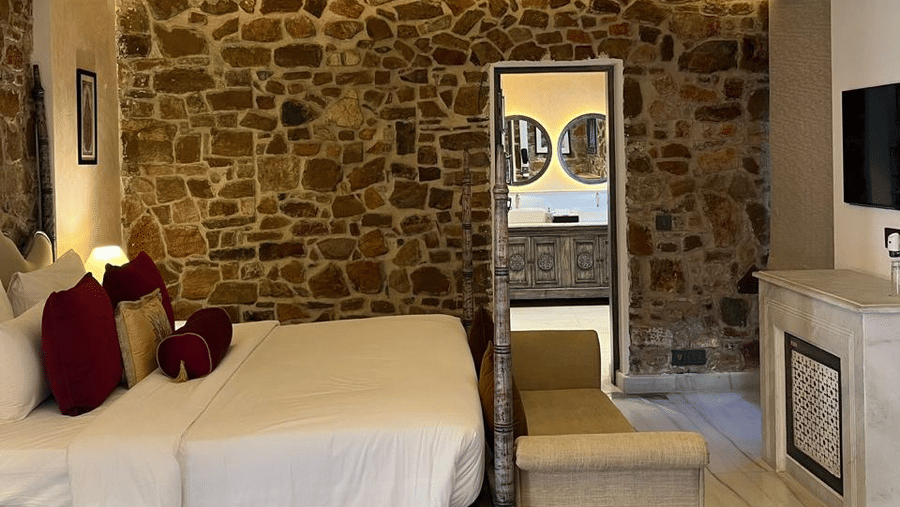 Spacious premium deluxe room at Juna Mahal with stone accent walls, stylish lighting and cosy bedding blending heritage charm with comfort.
