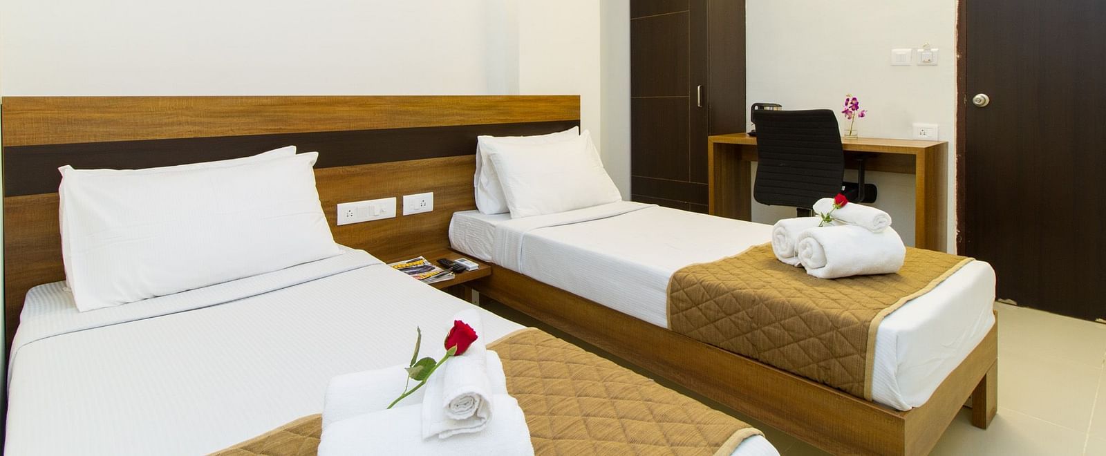 A hotel room including two single beds, a wardrobe, and a work desk and chair at Sanctum Suites Whitefield, Bangalore.