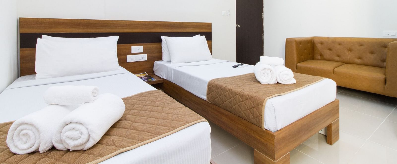 A room at Sanctum Suites Whitefield, Bangalore including twin beds with brown and white bedding and a sofa.