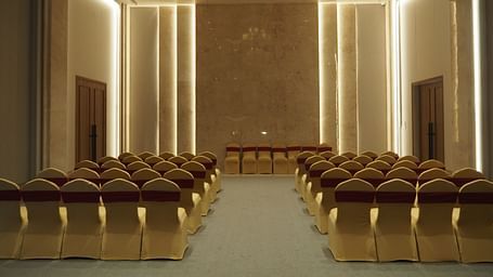 A grand hall with rows of chairs facing a stage, lit by a chandelier - Club Charholi, Pune 