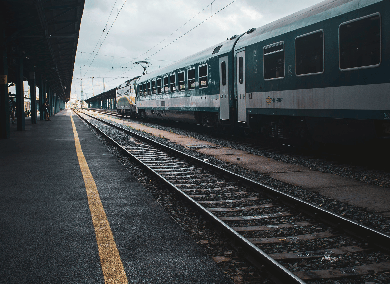 A stationary train on tracks is seen from the platform, with an overcast sky above.