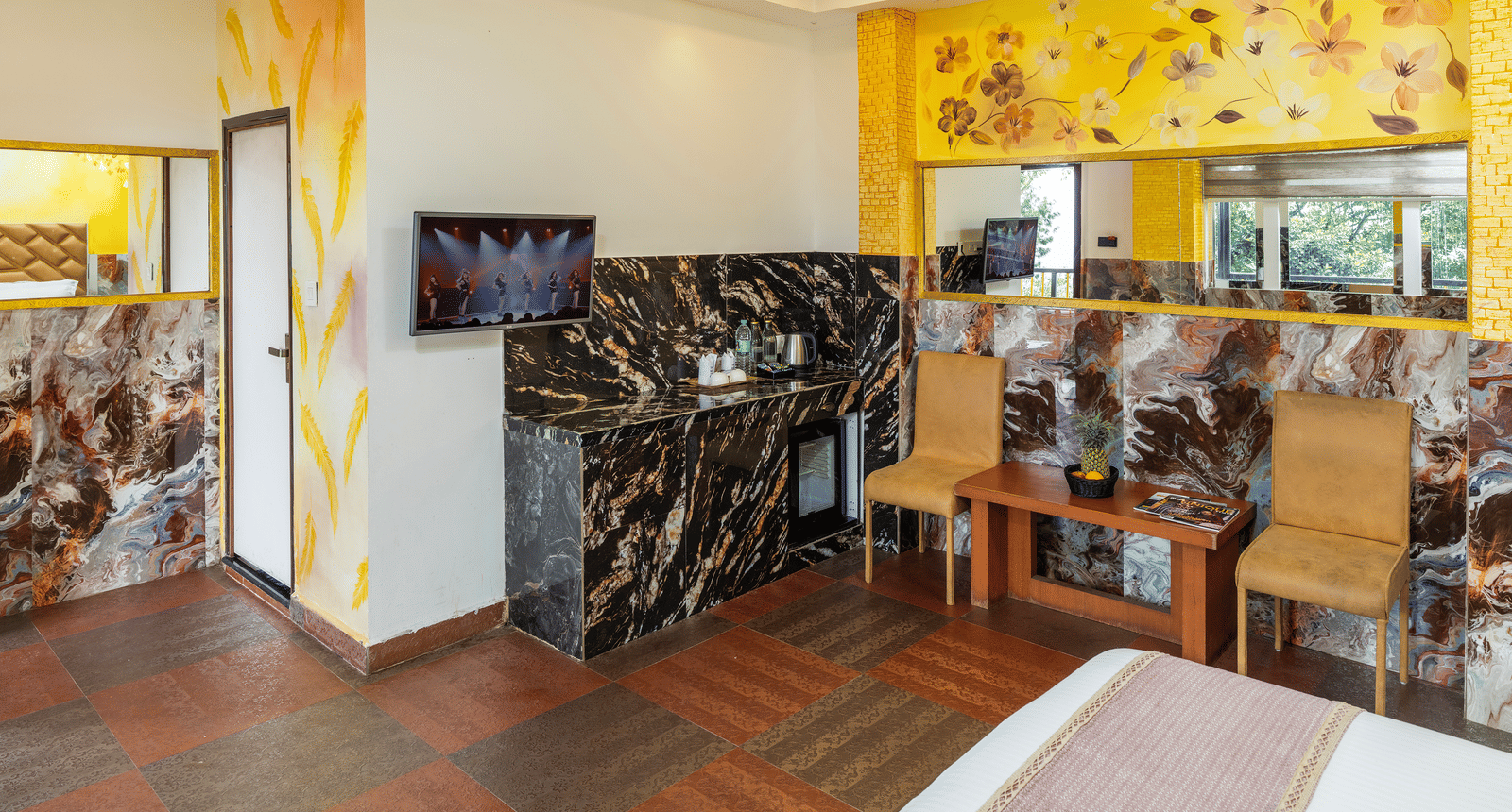 The Deluxe Non-AC Room at Parakkat Nature Hotel and Resorts, Munnar featuring a corner entertainment area, patterned walls, dark stone-like panelling, and an open doorway leading to the entrance or a different space.