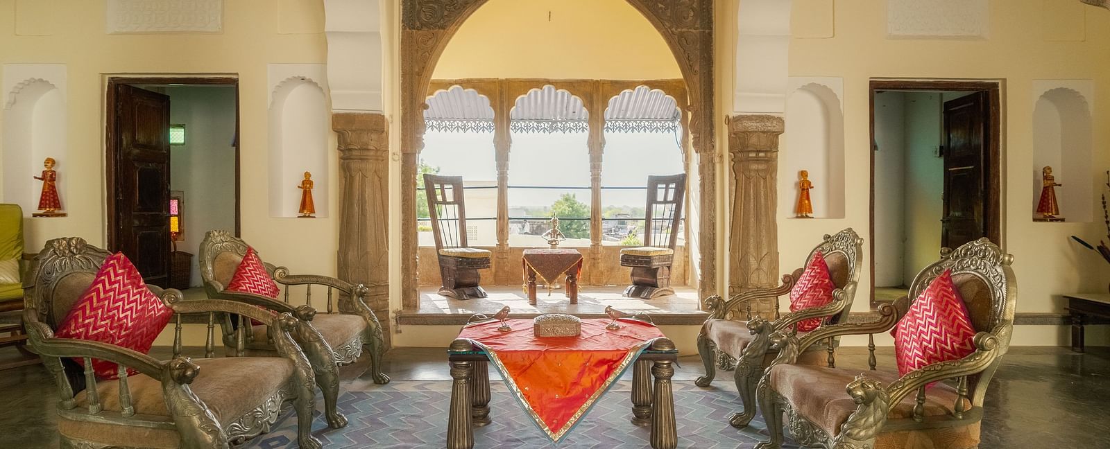 A richly decorated hallway at Fort Barli, illuminated with warm light, leads towards a grand wooden door.