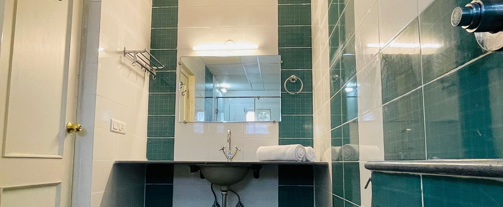 A bathroom featuring teal and white tiling and a sleek washbasin with a mirror at Sanctum Suites Indiranagar, Bangalore.