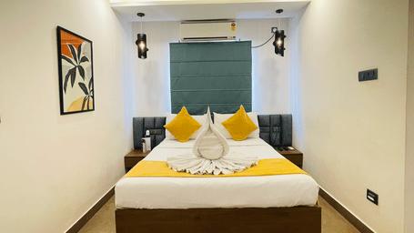King bed room at Hotel Kyzen Smart Stays Madhapur with yellow and white bedding, swan towel folding, teal headboard panel, wall sconces, and framed artwork above the bed.