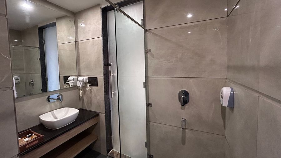 A shot taken from a higher angle of the washroom of the premium room featuring the wash basin, wall mounted mirror, and the shower area - DLS Grand Luxotica, Dehradun