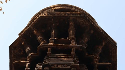 Ancient temple facade surrounded by lush green foliage, viewed from below with a clear blue sky in the background.