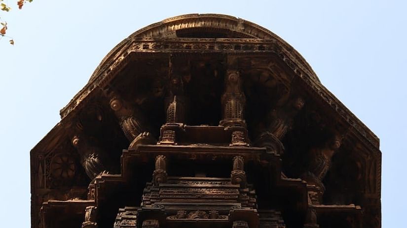 Ancient temple facade surrounded by lush green foliage, viewed from below with a clear blue sky in the background.