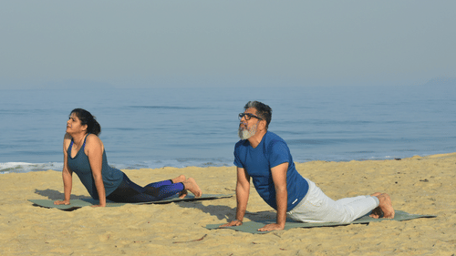 A couple performing Yoga on the beach with the sea in the background - Heritage Village Resort & Spa, Goa