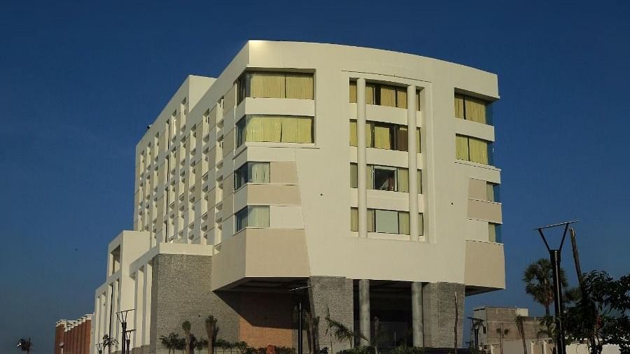 The exterior of Dhanalakshmi Srinivasan Hotels, Perambalur, at night, showing the illuminated building with light-coloured facades and a paved entrance leading to the main entrance, with streetlights on either side.