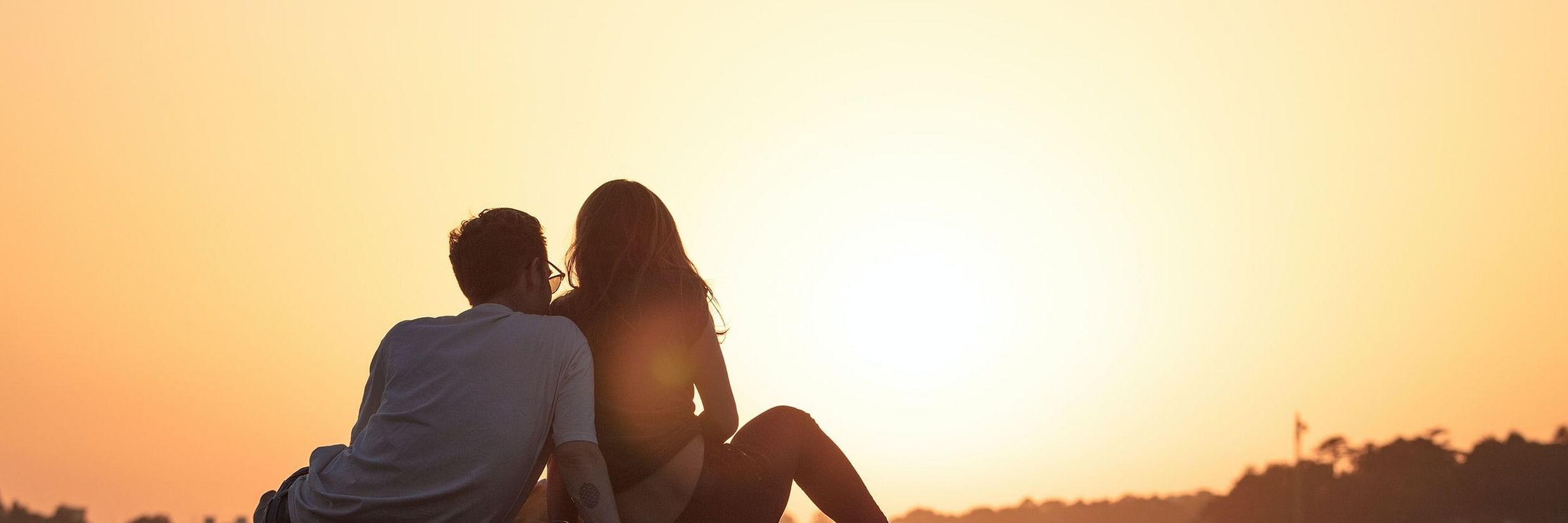 couple sitting on a pavement watching sunset.