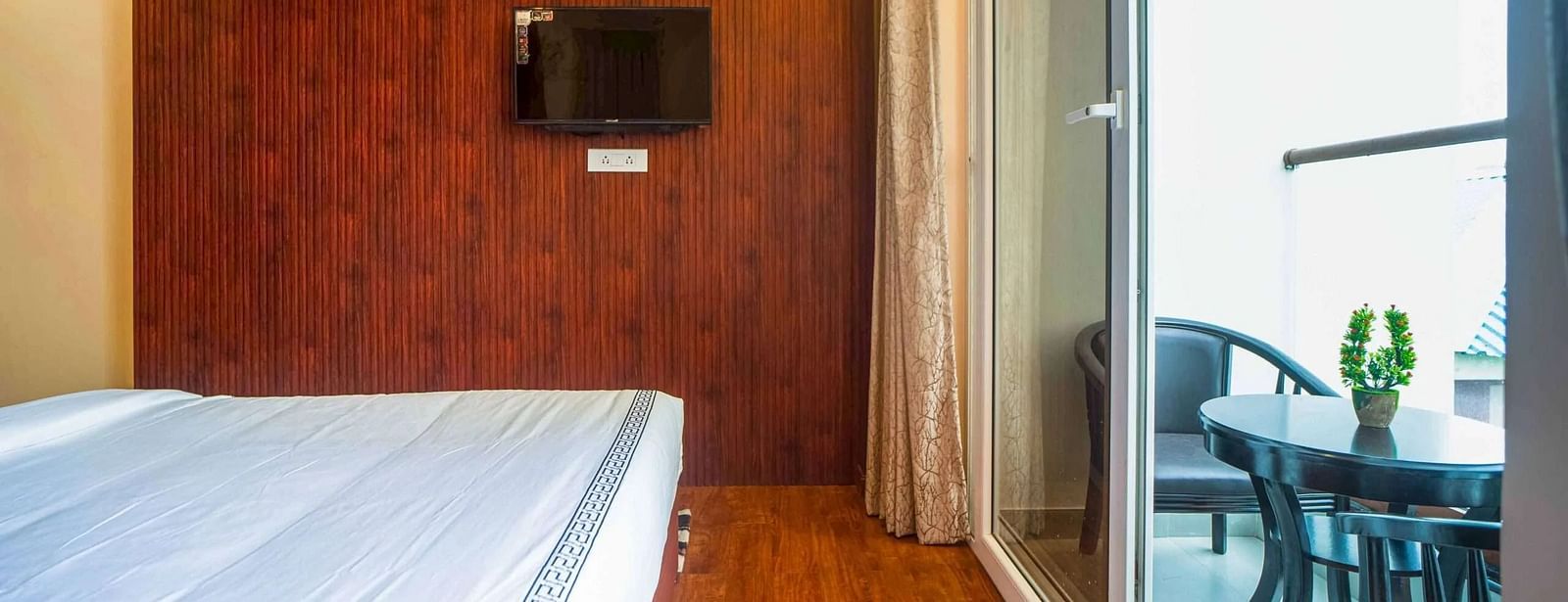 A comfortable room at Mansha Palace includes a bed, wooden flooring, a TV, and access to a balcony.