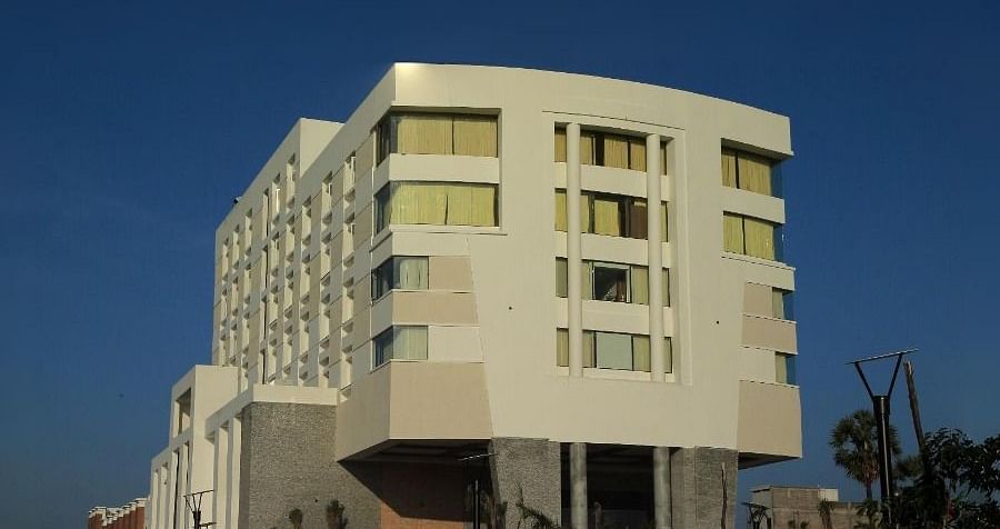 The exterior of Dhanalakshmi Srinivasan Hotels, Perambalur, at night, showing the illuminated building with light-coloured facades and a paved entrance leading to the main entrance, with streetlights on either side.