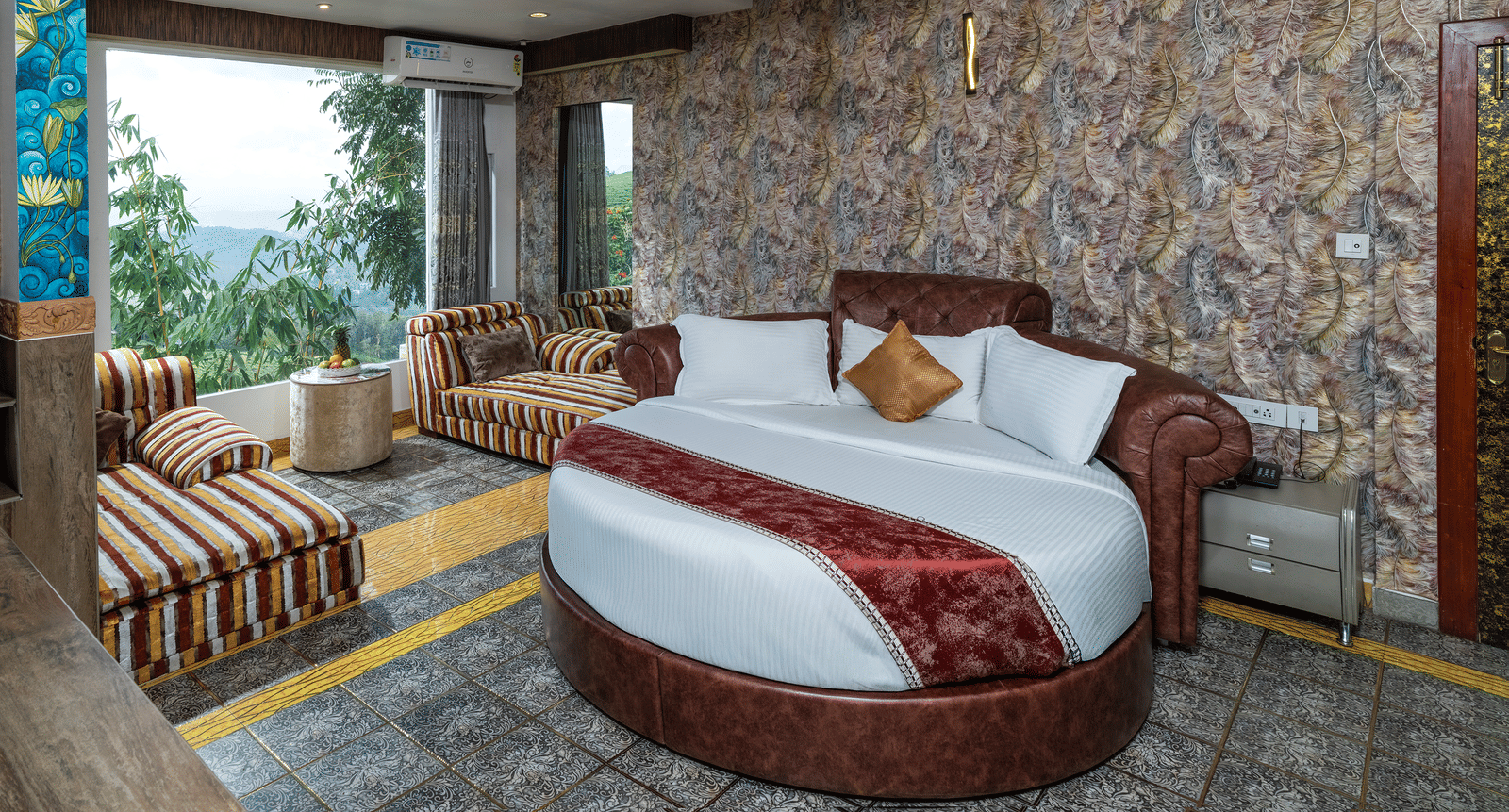 A bedroom in Family Jacuzzi Room featuring a round bed, a seating area beside large glass windows, and patterned walls.