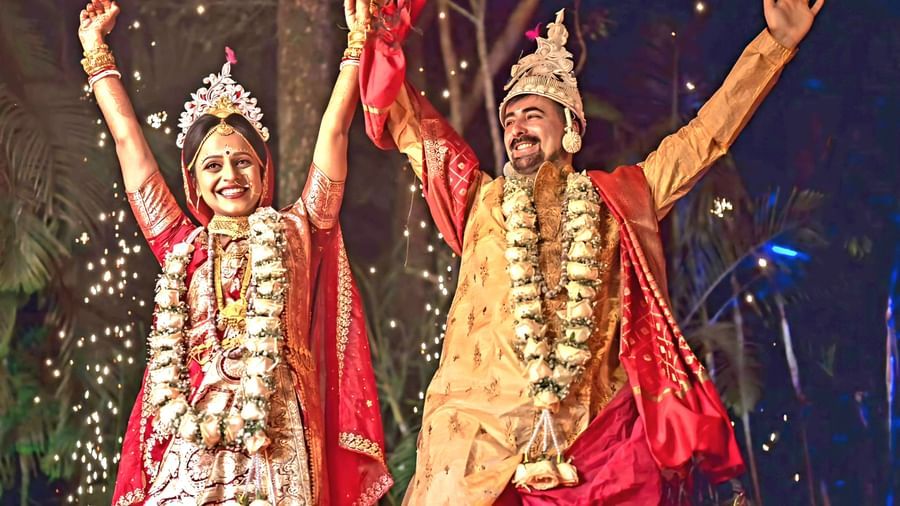 Two individuals in traditional Indian wedding attire raise their arms in celebration during a ceremony