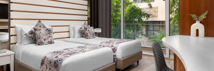  Contemporary room at The Atara, Gurugram featuring two single beds, a white desk, and a balcony view. The room has light wood floors and horizontal wall decor