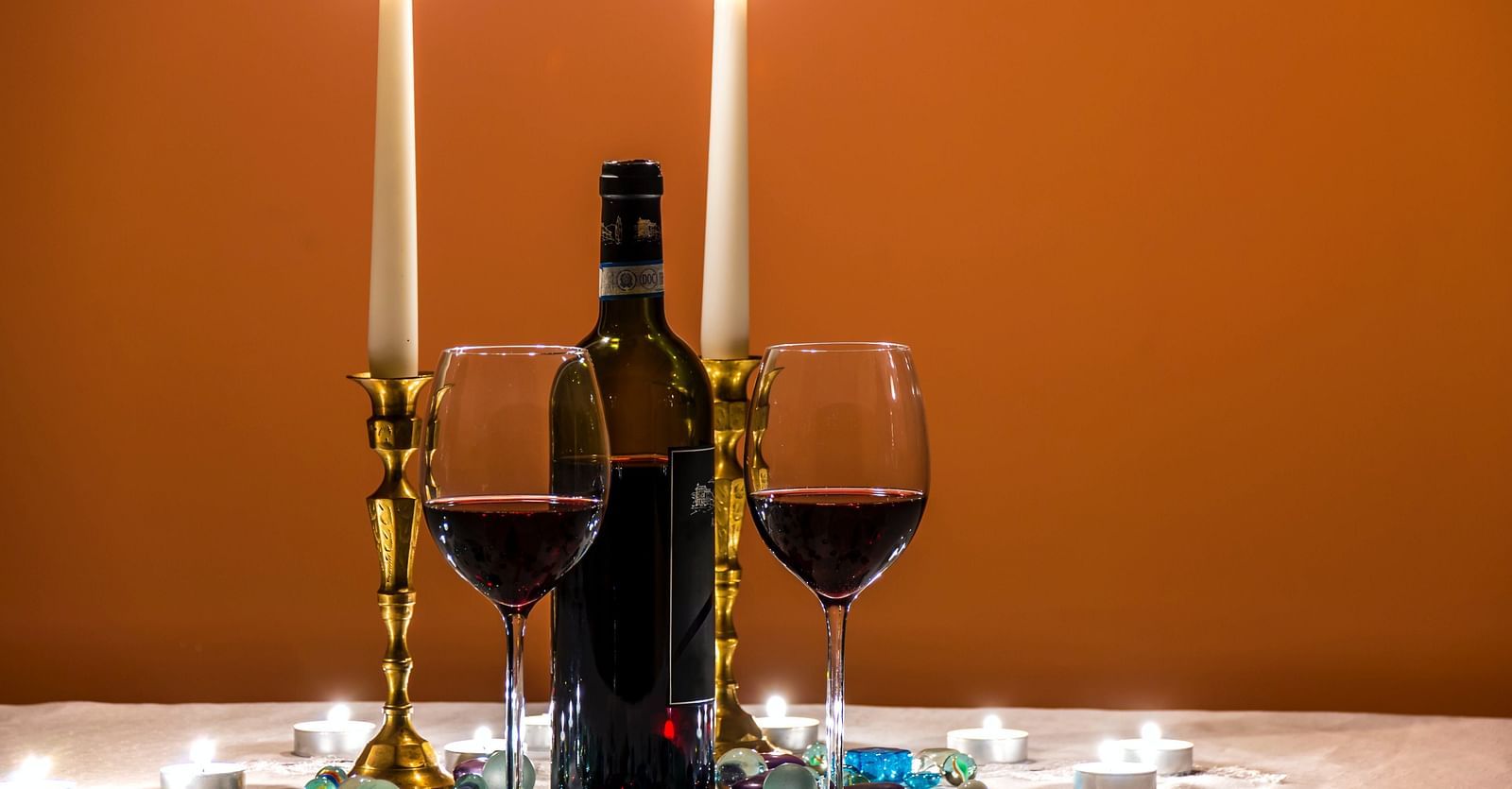 a candlelight dinner with two glasses of wine, two lit candles and a wine bottle in view