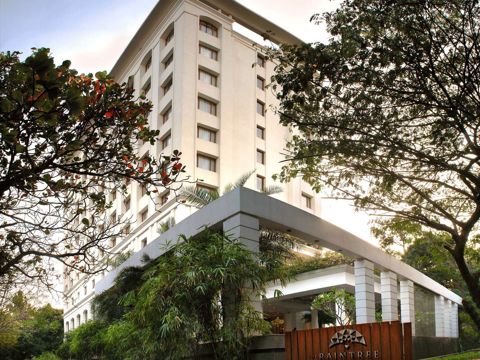 Facade view of The Raintree, St. Mary's Road - Hotel Near Chennai Trade Centre, surrounded by greenery under a vibrant sky