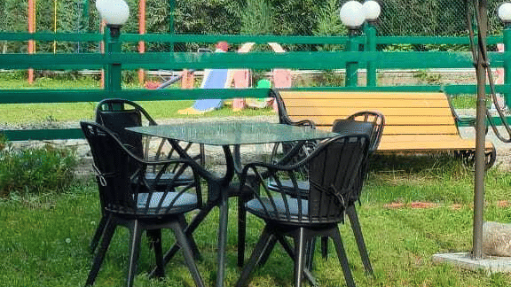 A vertical view showing an outdoor seating arrangement with a table and chairs set on a grassy lawn under a canopy umbrella.