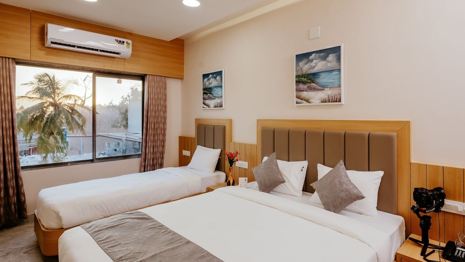 Corner view of a spacious Pride Room at Daksh The Grand Gowardhan, Dwarka, with multiple beds, modern decor, and a window with views.