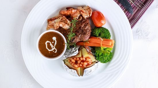 A plated dish features meat, vegetables, and a sauce drizzle on a white plate, presented with a patterned cloth.