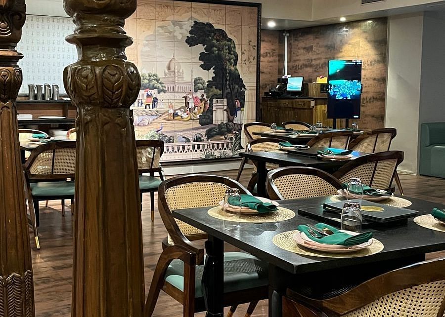 Elegant restaurant interior featuring set tables with place settings, ornate columns, and a large mural on the back wall - Astra Hotels & Suites, Spice Garden Layout