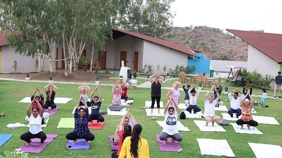 Outdoor yoga class on a lawn with a group of people following an instructor.- Bamboo Saa, Udaipur