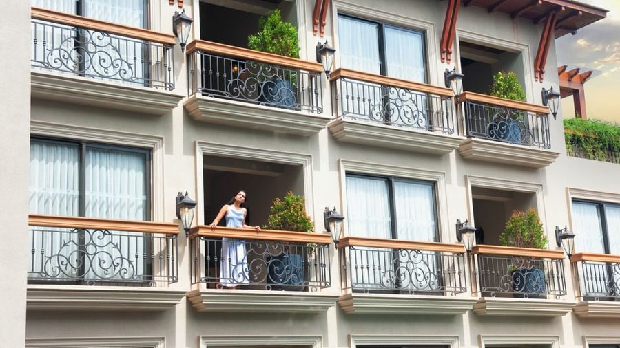 A woman standing in the balcony looking at the surrounding as she leans against the railing at The Evren, Vagator.