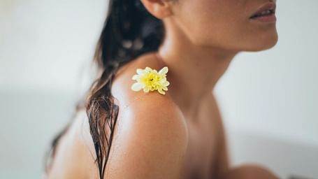 A lady sitting with her knees up, her body wet, and a flower resting on her shoulder