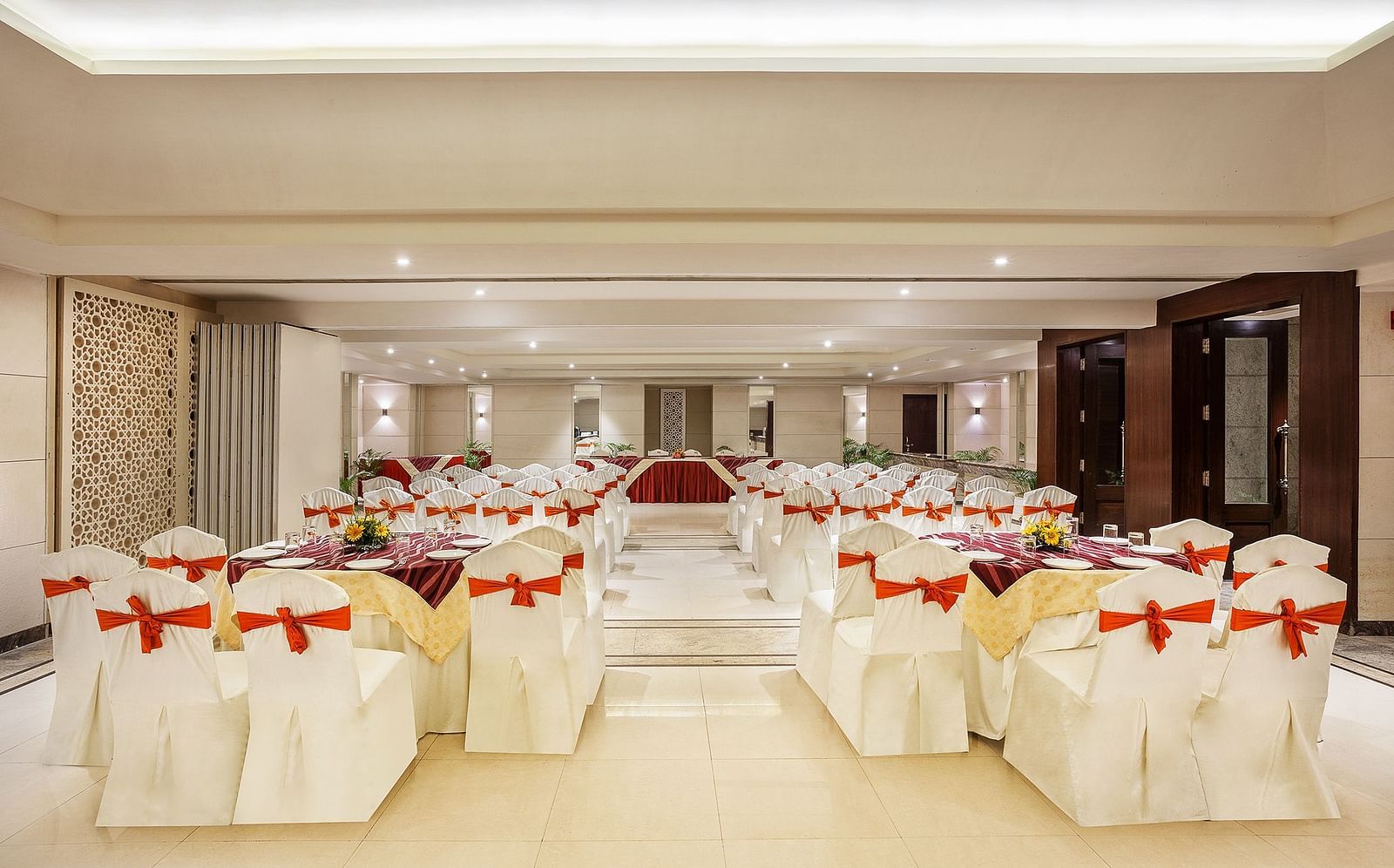 an image of an event space showing a well-spaced seating arrangement with white chairs tied with red bows - The Manor, Bareilly